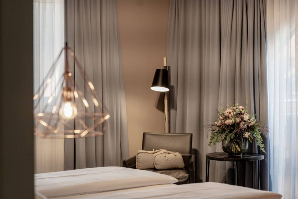Un dormitorio con una cama, una silla, una lámpara y un florero con flores.