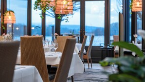 Un restaurante con sillas de mimbre, manteles blancos y lámparas colgantes de mimbre.