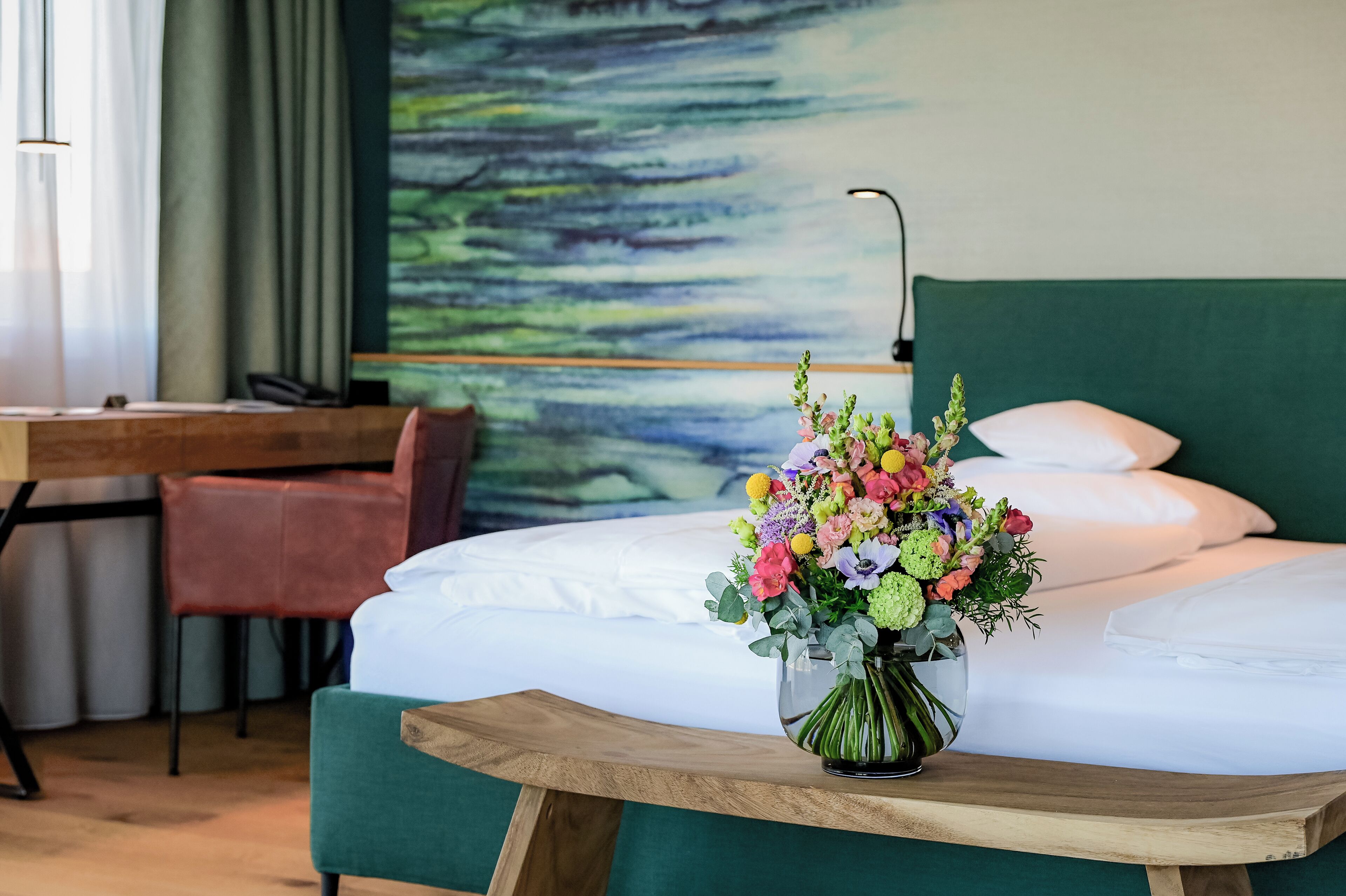 Een hotelkamer met een bed, een bureau, een stoel en een bloevas.