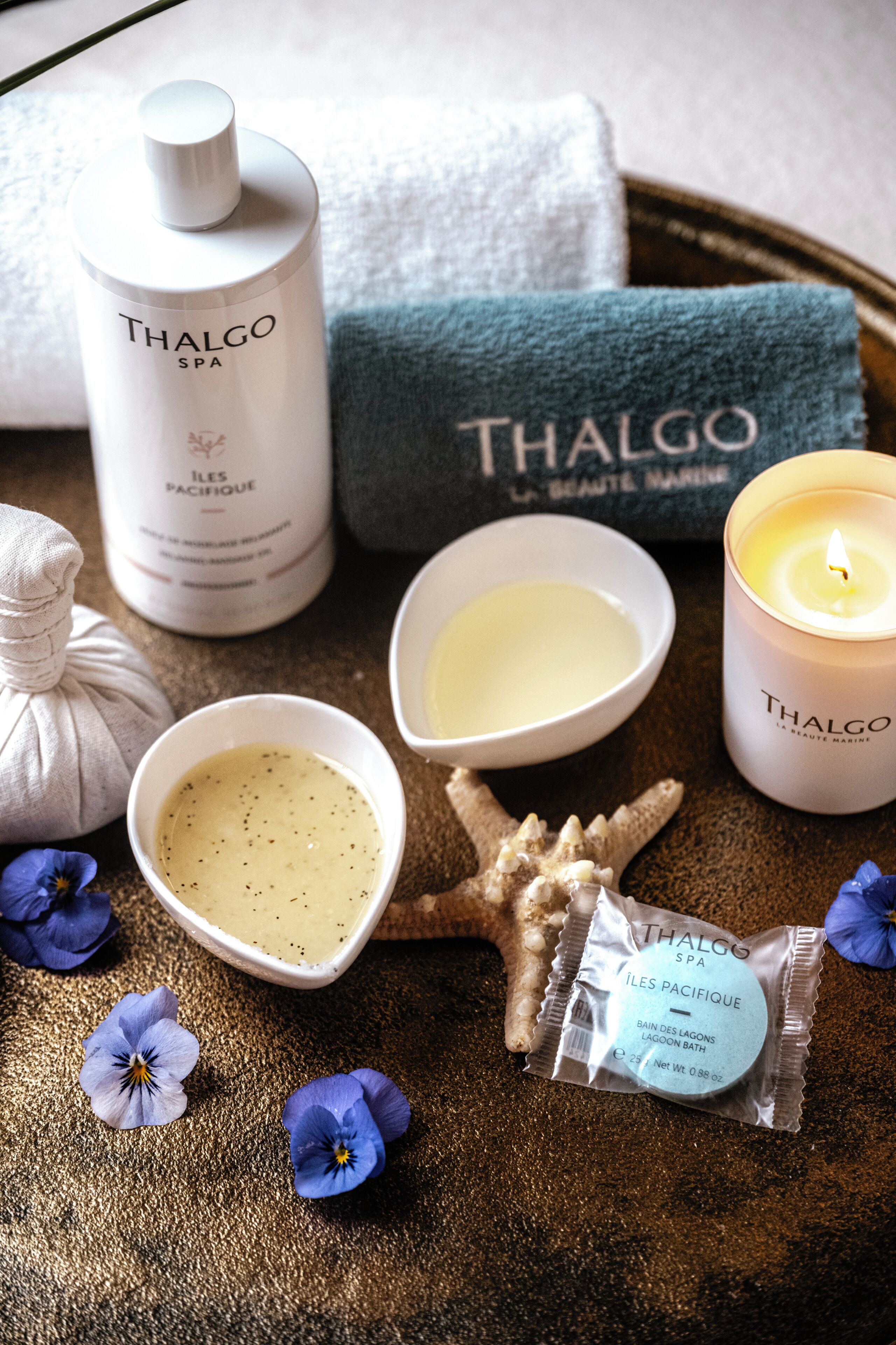 A tray with Thalgo SPA products, a candle, a starfish, and blue flowers.