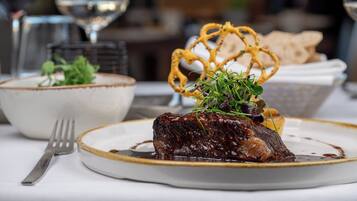 A plate of food with a piece of meat, a bowl, and a fork on a table.