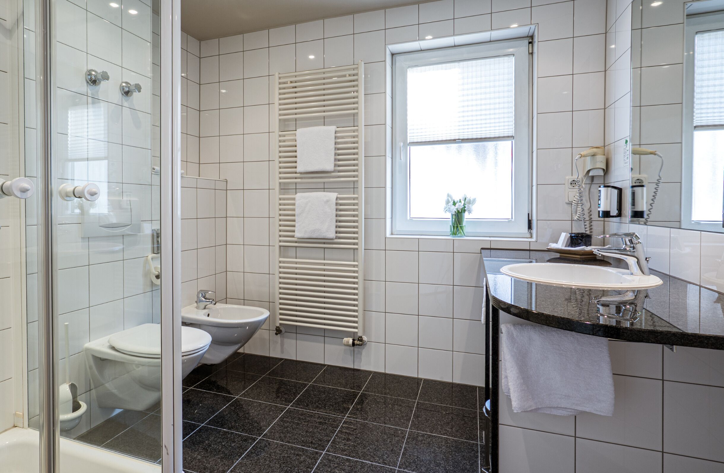 A modern bathroom with a glass shower enclosure, a toilet, bidet, and a sink with a vanity.