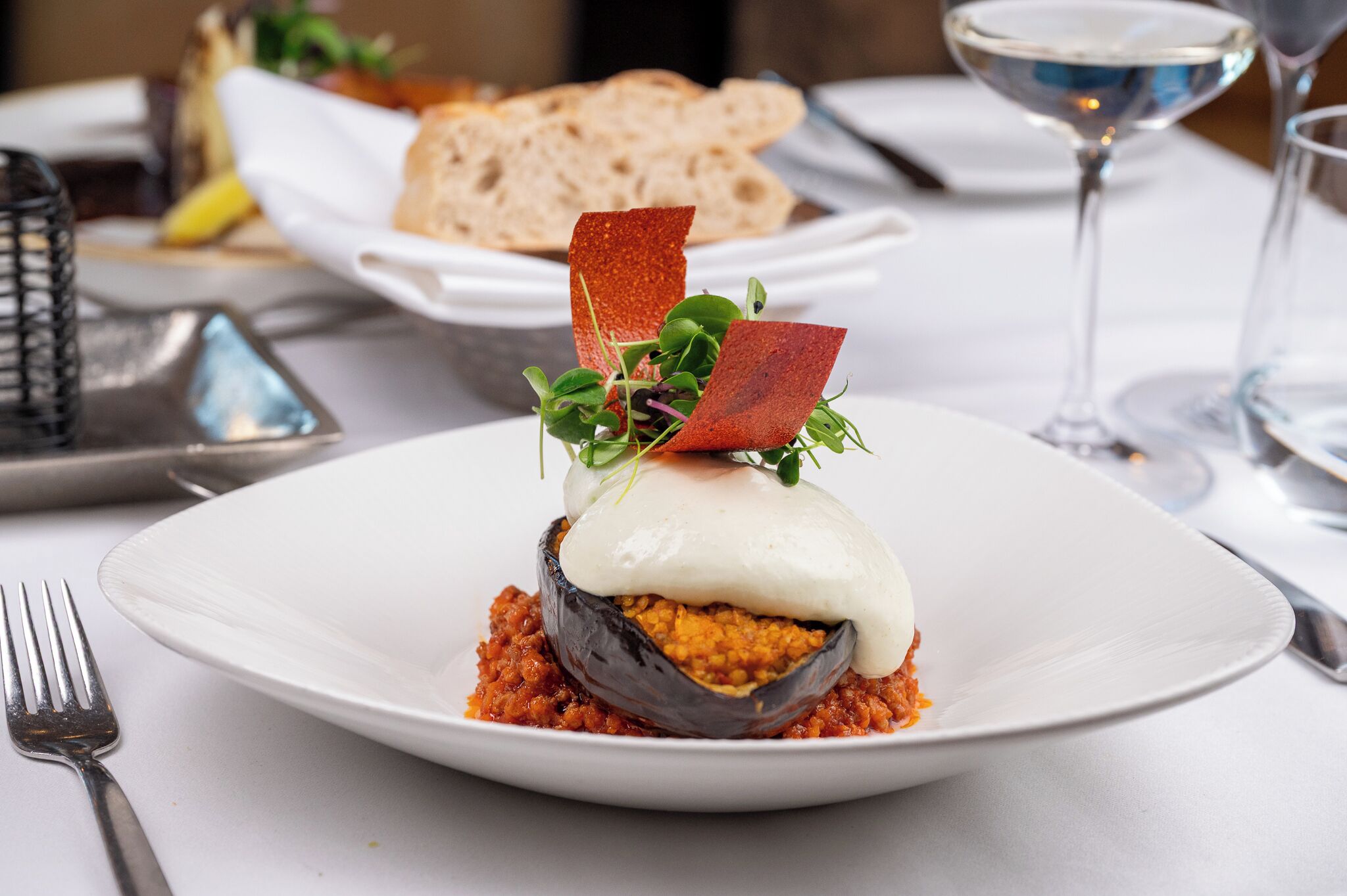 A plate with a stuffed eggplant dish, a fork, and a glass of water on a table.