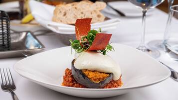 A plate with a stuffed eggplant dish, a fork, and a glass of water on a table.