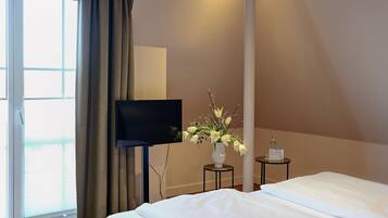 A hotel room with a bed, a TV, a vase with flowers, and a small table with a bottle.