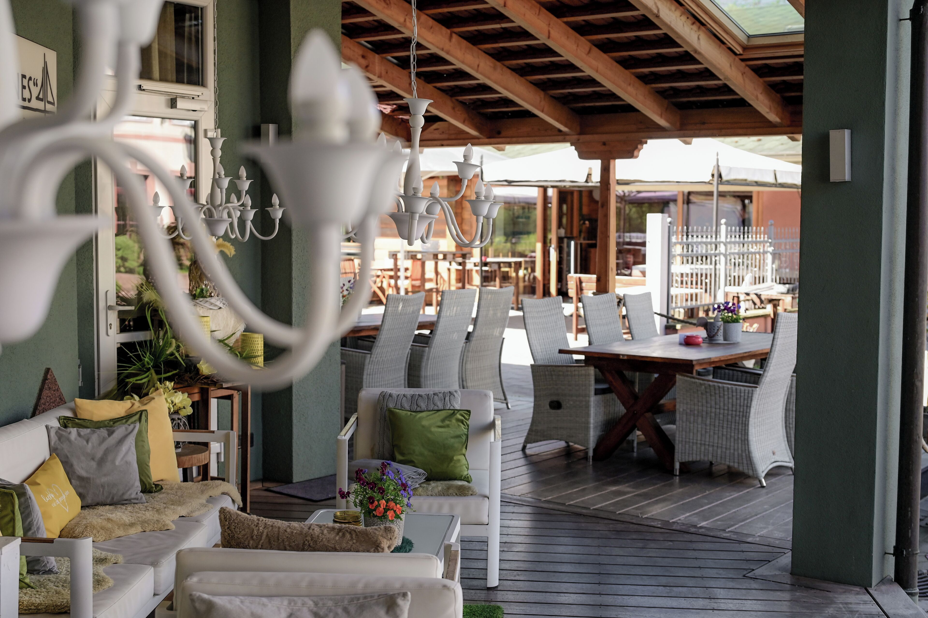 A covered outdoor seating area with wicker furniture, a chandelier, and a view of the interior.