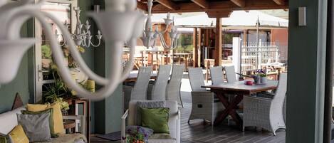 A covered outdoor seating area with wicker furniture, a chandelier, and a view of the interior.