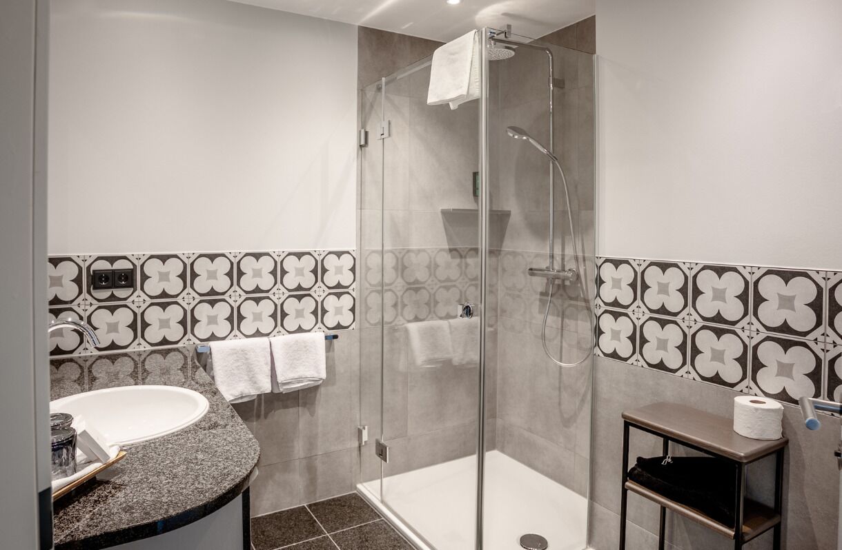 A modern bathroom with a glass-enclosed shower, a sink, and a small table with a towel and a bottle.