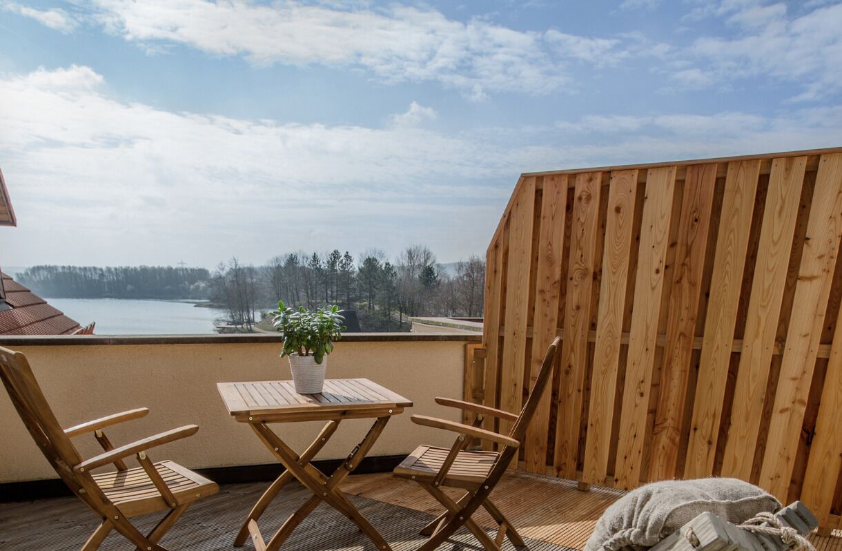 A wooden deck with a table and chairs, a potted plant, and a view of a lake.