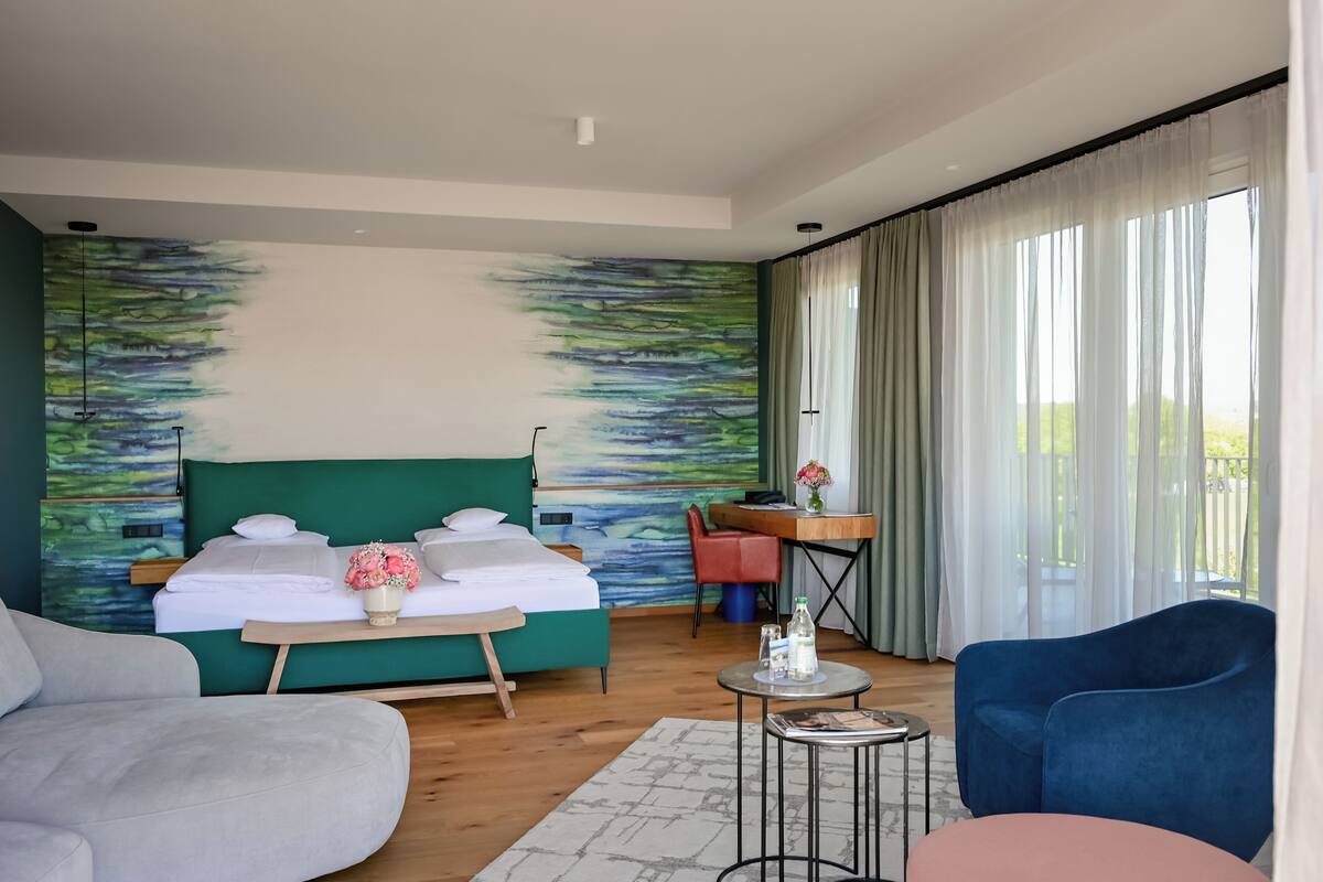 Habitación de hotel con cama, escritorio, silla, sofá y vista a espacios verdes.