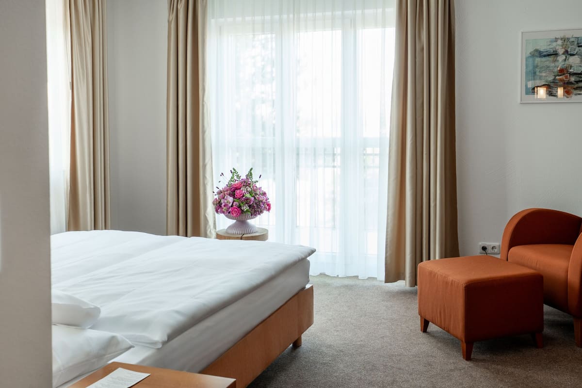 Habitación de hotel con cama, una mesita con un jarrón de flores, una silla y un cuadro en la pared.