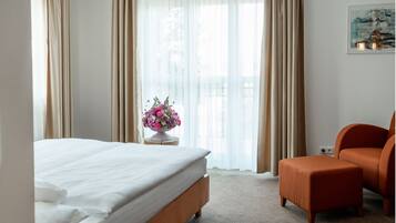 Une chambre d’hôtel avec un lit, une petite table sur laquelle est posé un vase de fleurs, une chaise et un tableau accroché au mur.