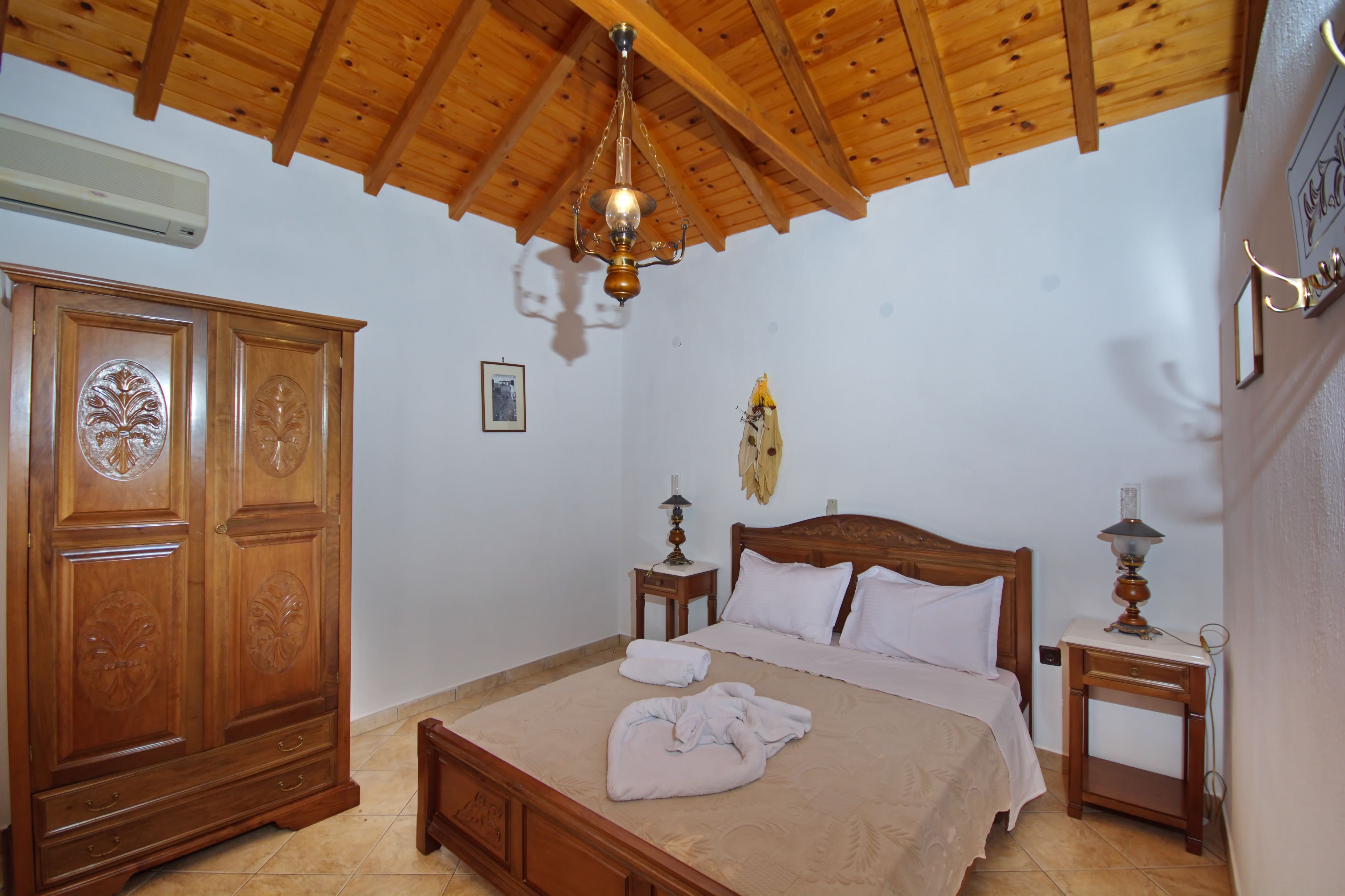 A bedroom with a wooden bed, a wardrobe, a chandelier, and a bedside table with a lamp.