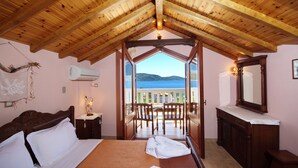 A bedroom with a wooden ceiling, a bed with white linens, a wooden dresser, and a view of the sea through a balcony door. - Pelagos Villas (Alonissos)
