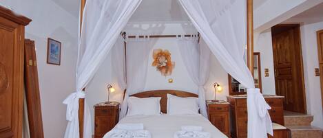 A four-poster bed with white drapes, two bedside tables with lamps, and a wooden headboard.
