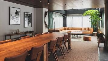 A modern meeting room with a long wooden table, leather chairs, a sofa, and a large window with curtains.