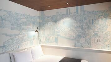 A hotel room with a cityscape mural, a white bed with pillows, and a wooden ceiling.