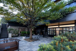 An outdoor seating area with benches and tables, surrounded by trees and plants. - TRUNK (HOTEL) CAT STREET (Tokyo)