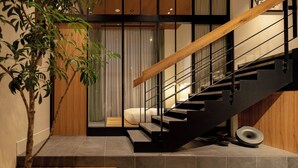 Una escalera moderna con barandilla de madera y pasamanos metálicos, que conduce a una habitación con cama y un gran ventanal con cortinas.