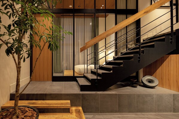 A modern staircase with a wooden handrail and metal balusters, leading to a bedroom with a bed and a window with curtains. - TRUNK (HOTEL) CAT STREET (Tokyo)