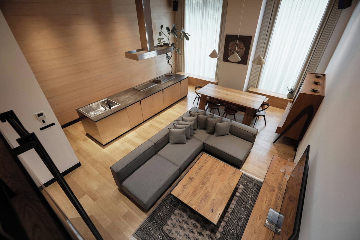 A modern kitchen with a built-in island, a dining area with a wooden table, and a living space with a sectional sofa.