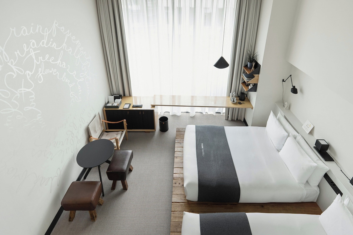 A modern hotel room with a bed, a desk, a chair, and a small table.