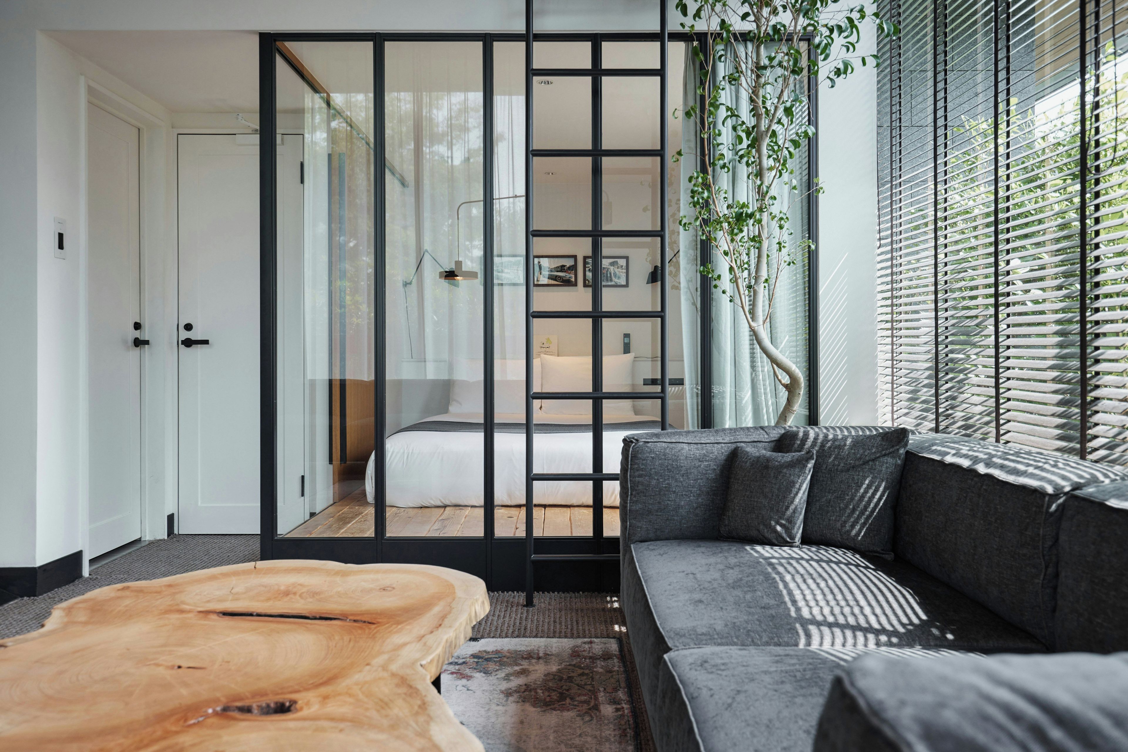 Un interior moderno con un sofá, una mesa de centro de madera y un ventanal corredero que da a un dormitorio.