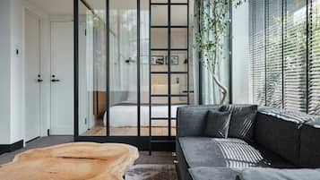 A modern interior with a sofa, a wooden coffee table, and a sliding glass door leading to a bedroom.