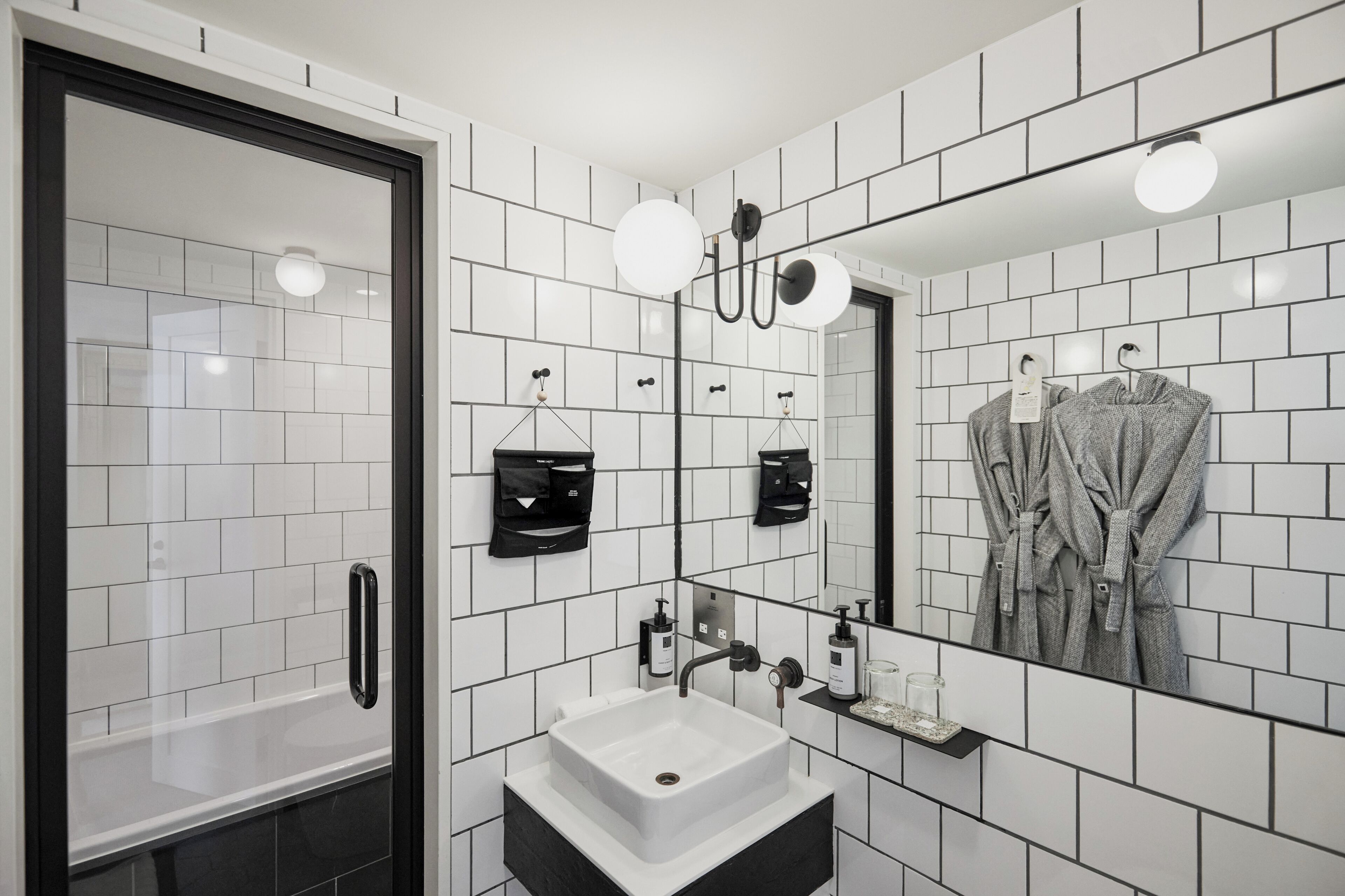 A modern bathroom with a large mirror, white tiles, a sink, and a shower.