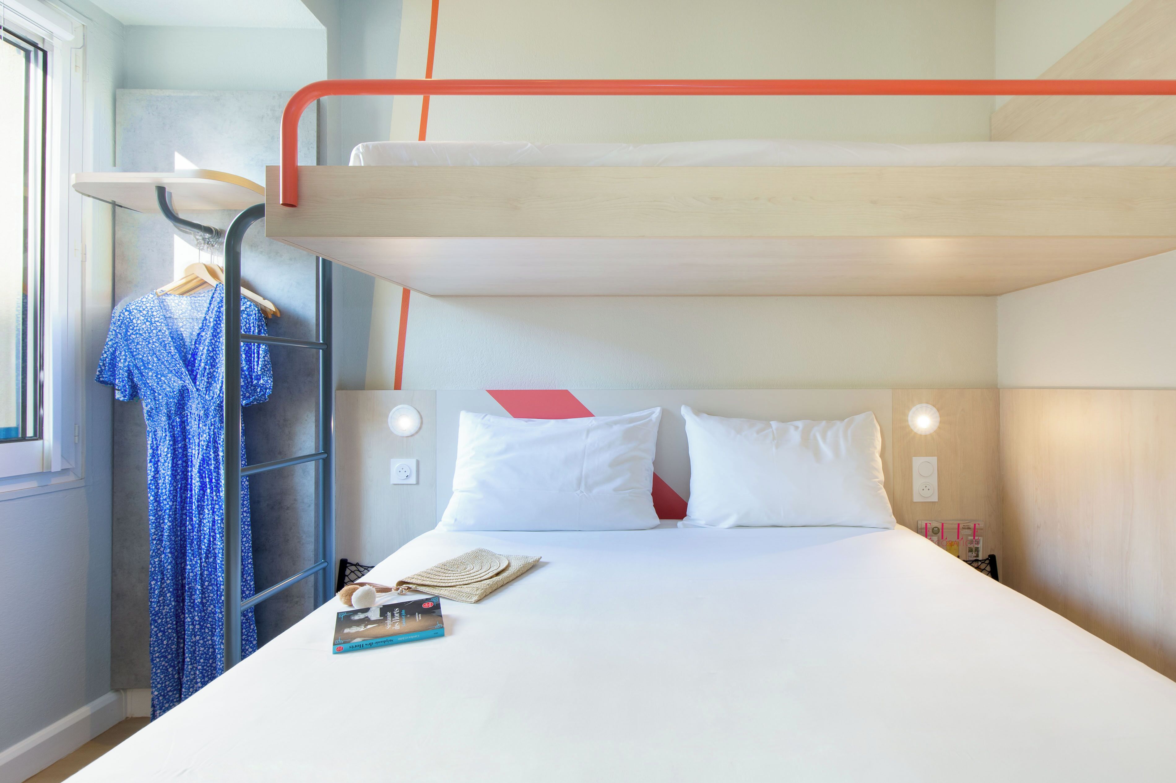 A bunk bed with a red ladder, a white bedspread, and a blue patterned garment hanging on a rack.