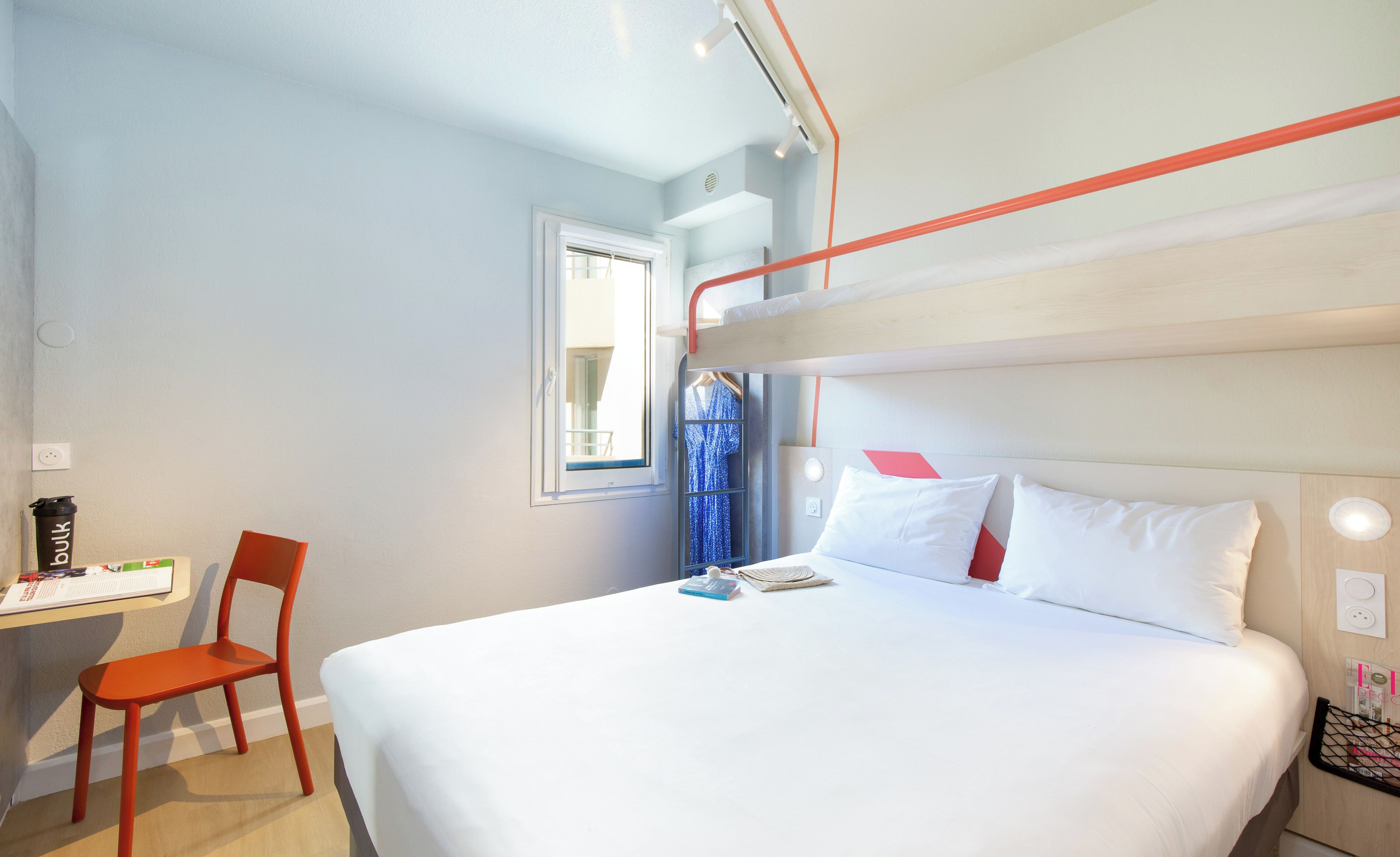 A bunk bed with white bedding, a desk with a chair, and a window with a view.
