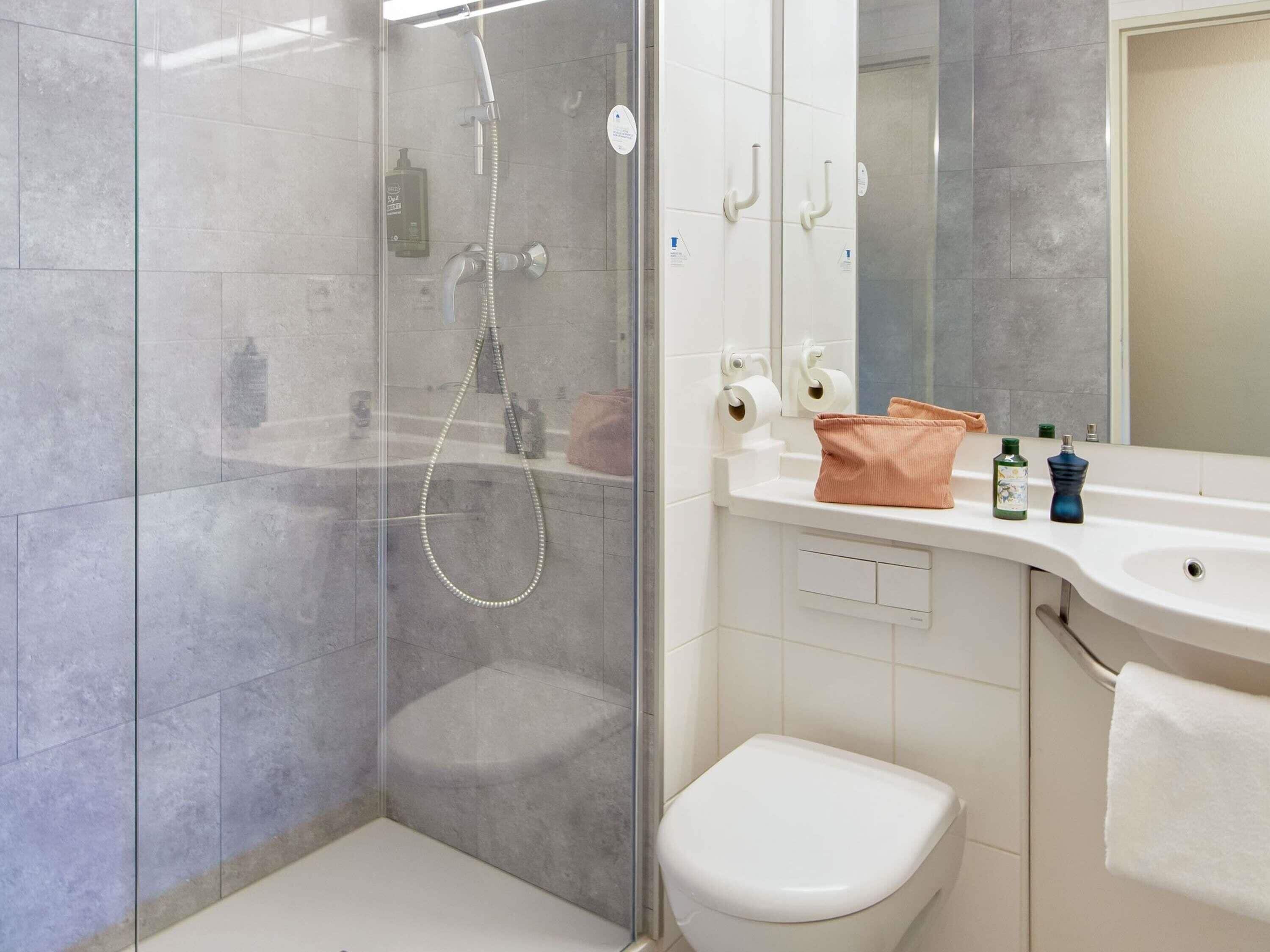 Een moderne badkamer met een douchecabine van glas, een wit toilet en een wastafel met toiletartikelen.