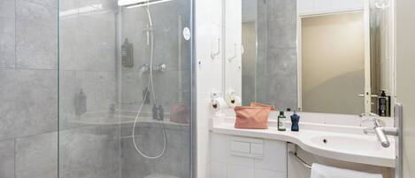 A modern bathroom with a glass-enclosed shower, a white toilet, and a sink with a mirror above it.