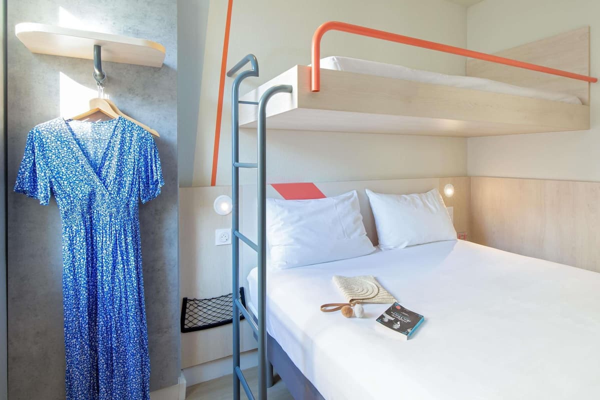 Een slaapkamer met stapelbed, een hangende jurk, een boek en een wandlamp.