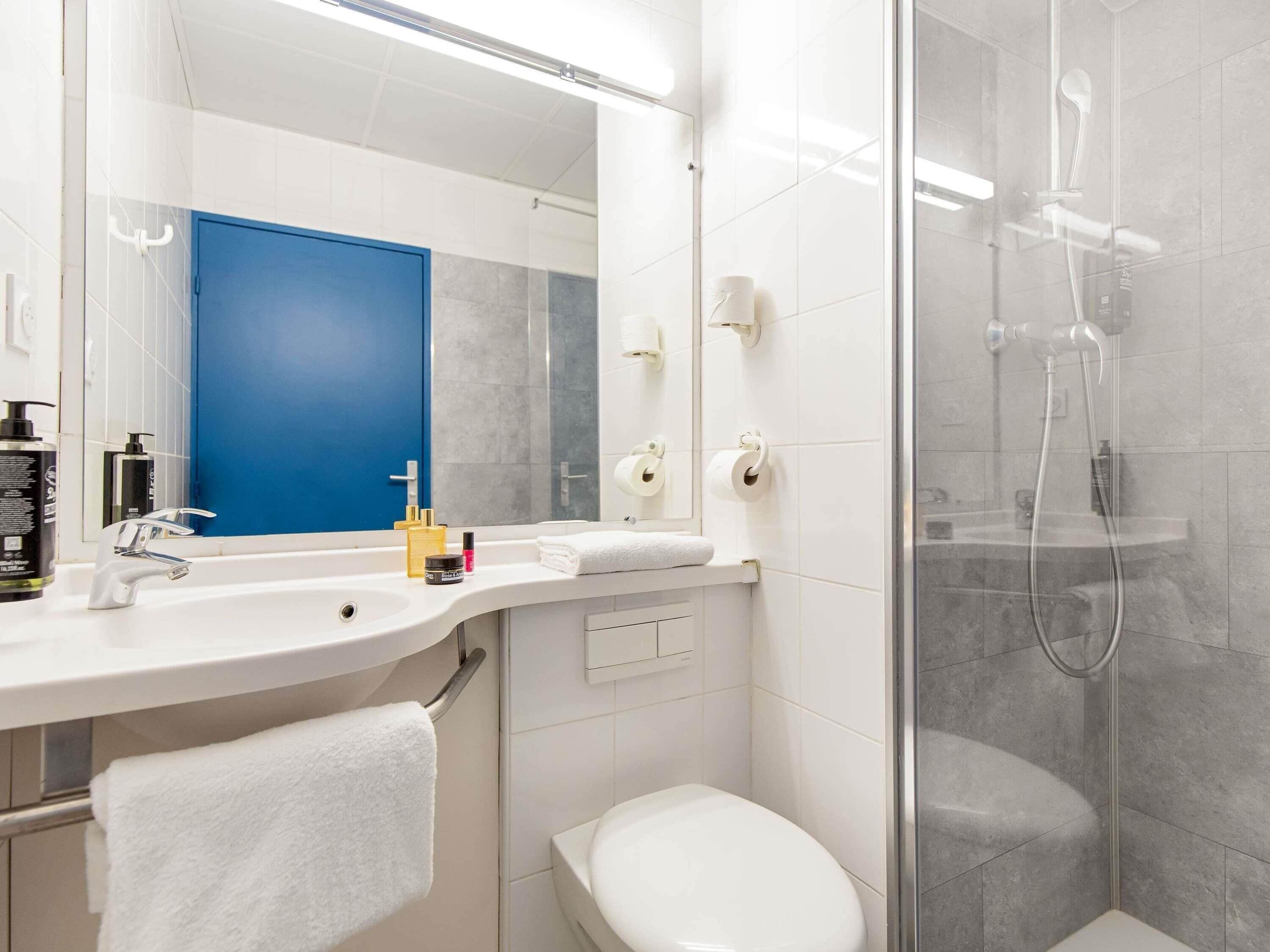 Un baño con lavamanos blanco, espejo, inodoro y ducha.
