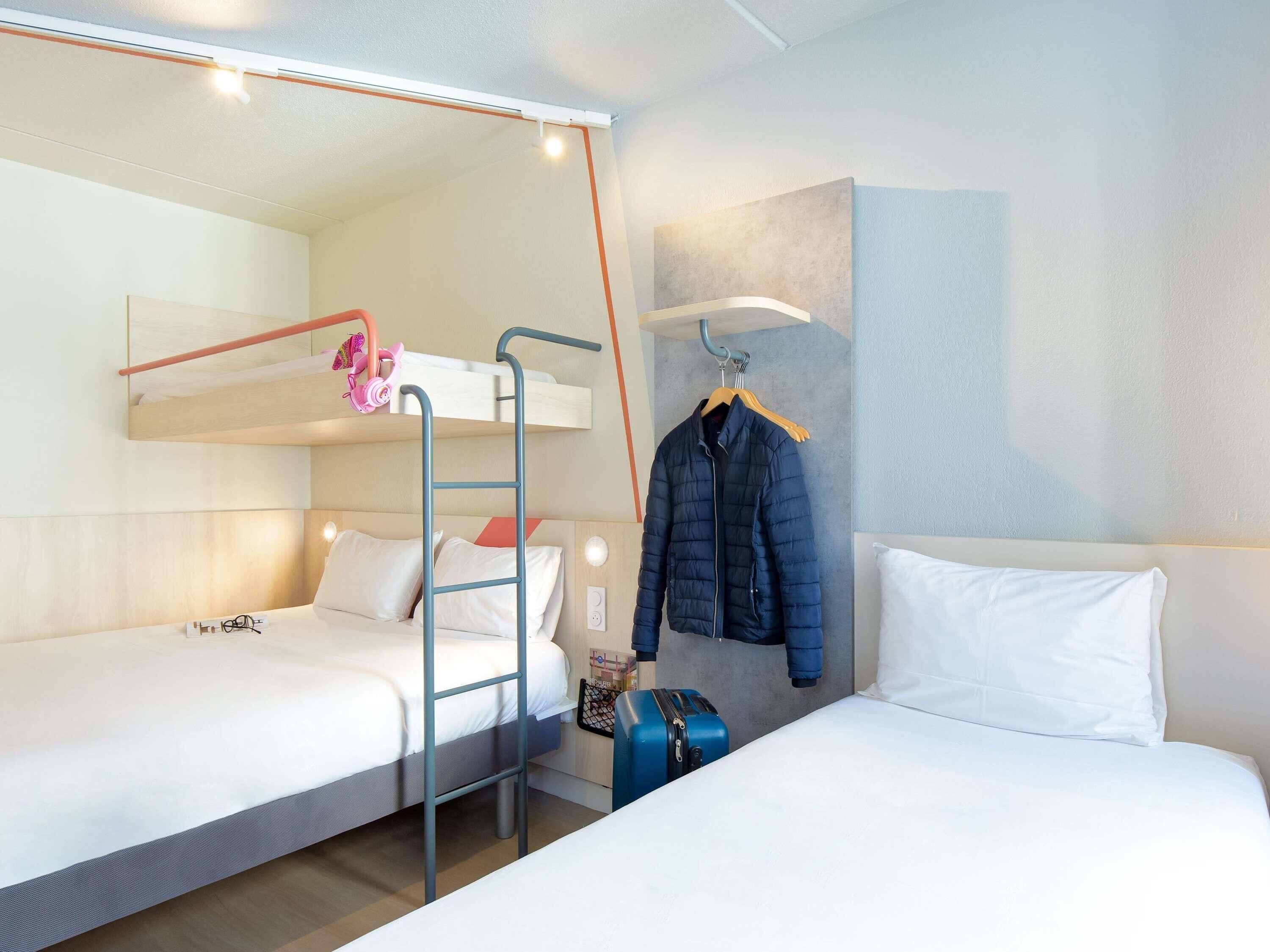 A hotel room with bunk beds, a ladder, a hanging coat rack, and a suitcase.