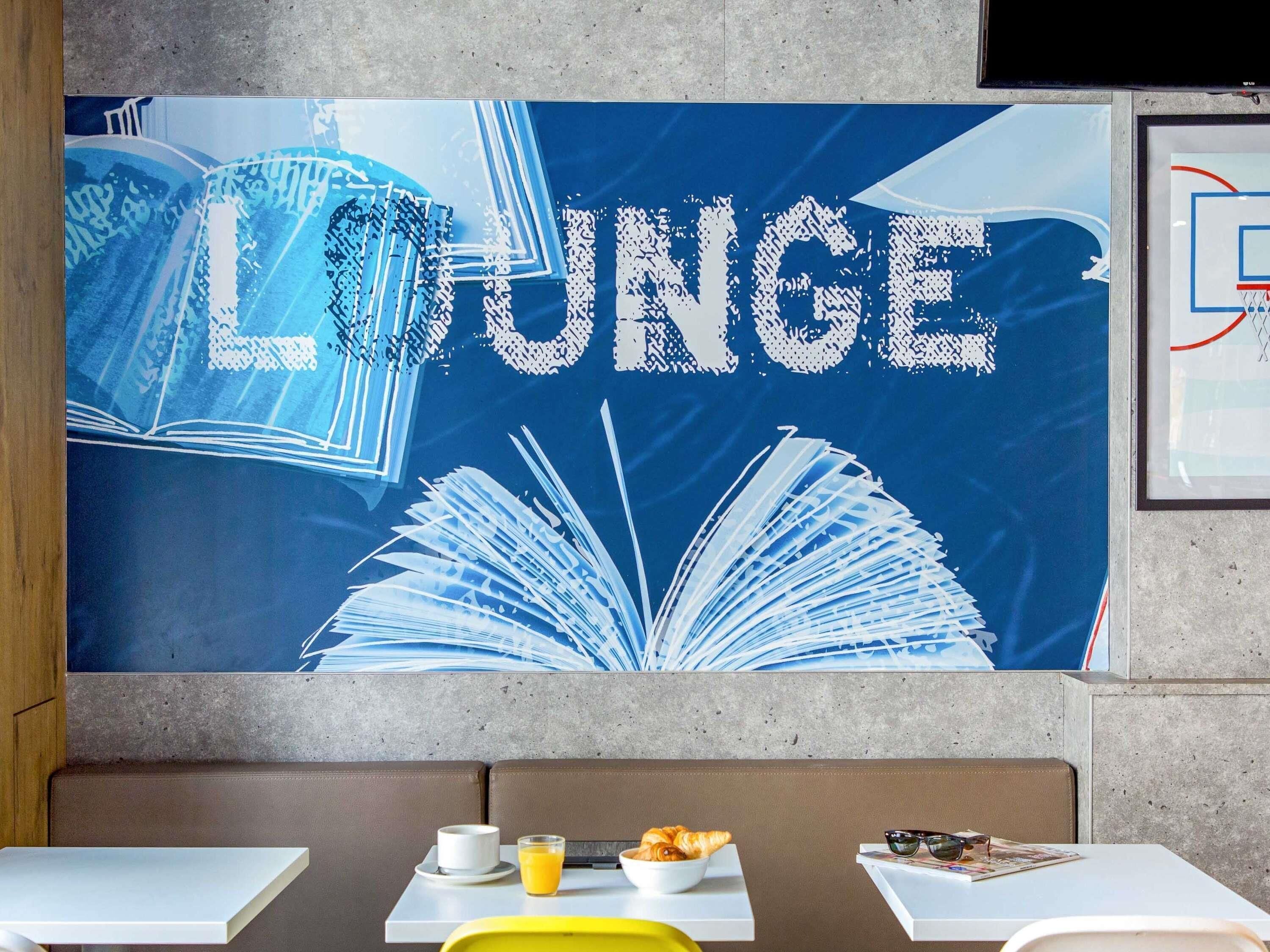 Un espacio de sala de estar con un gran mural en la pared que presenta libros y la palabra 'LOUNGE' escrita en grande.