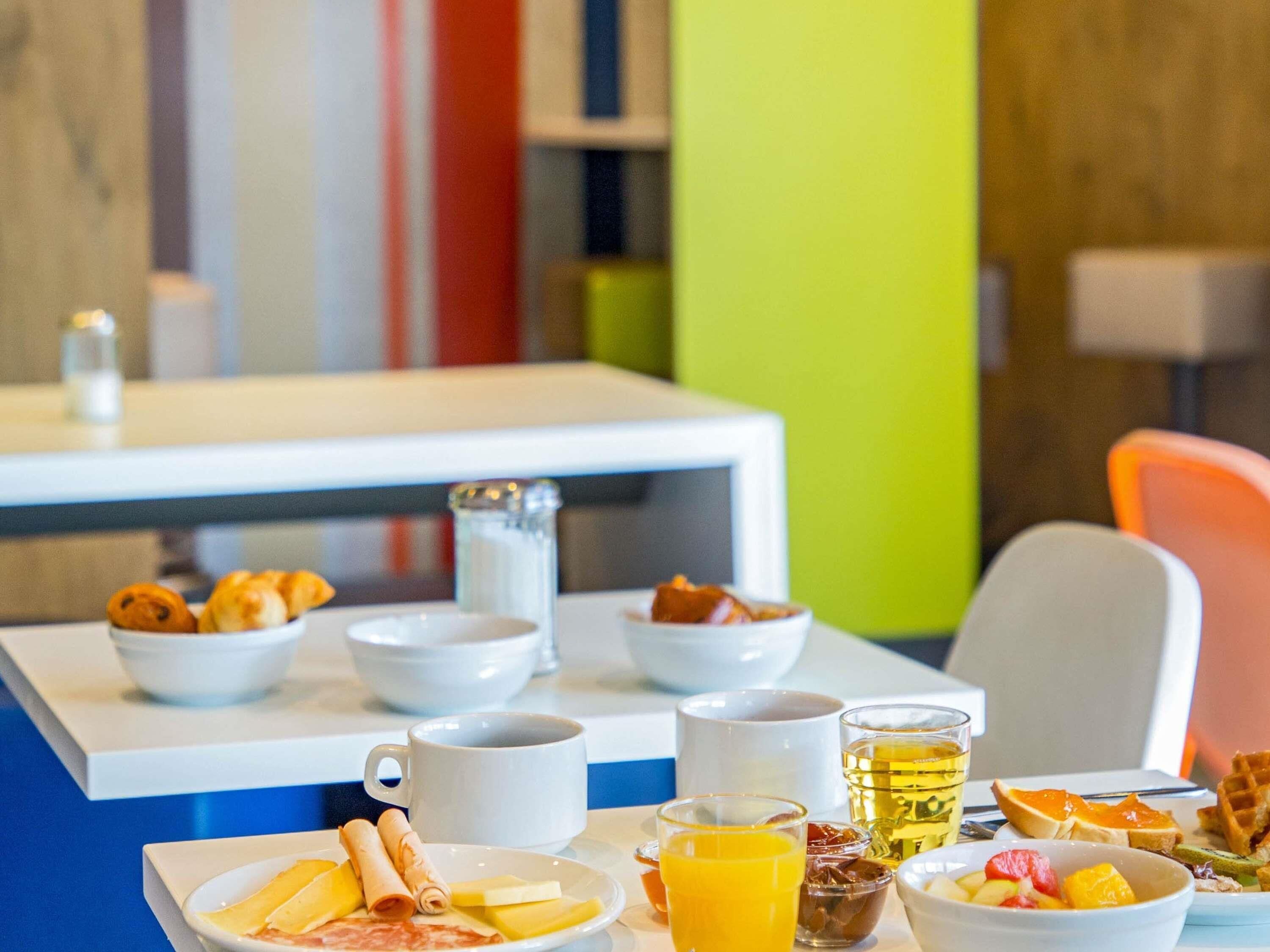 A breakfast table with various food items, a coffee pot, and a glass of orange juice.
