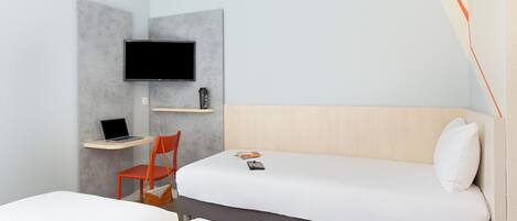 Habitación de hotel con cama, escritorio con laptop, una silla, televisor montado en la pared y mesita de noche con control remoto.