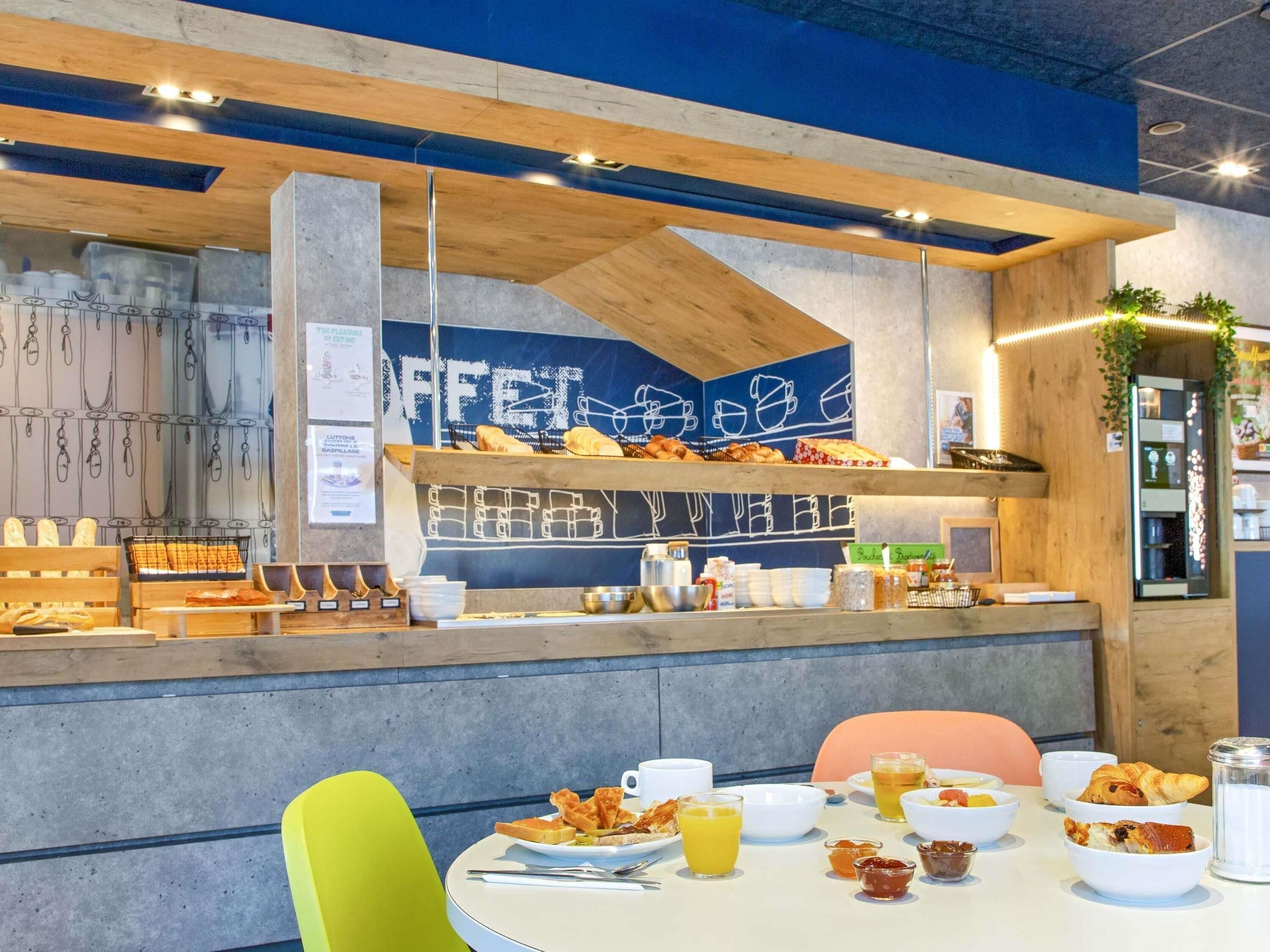 Un espace dédié au petit-déjeuner, avec un comptoir où sont exposées des pâtisseries et un coin salon comprenant des tables et des chaises.