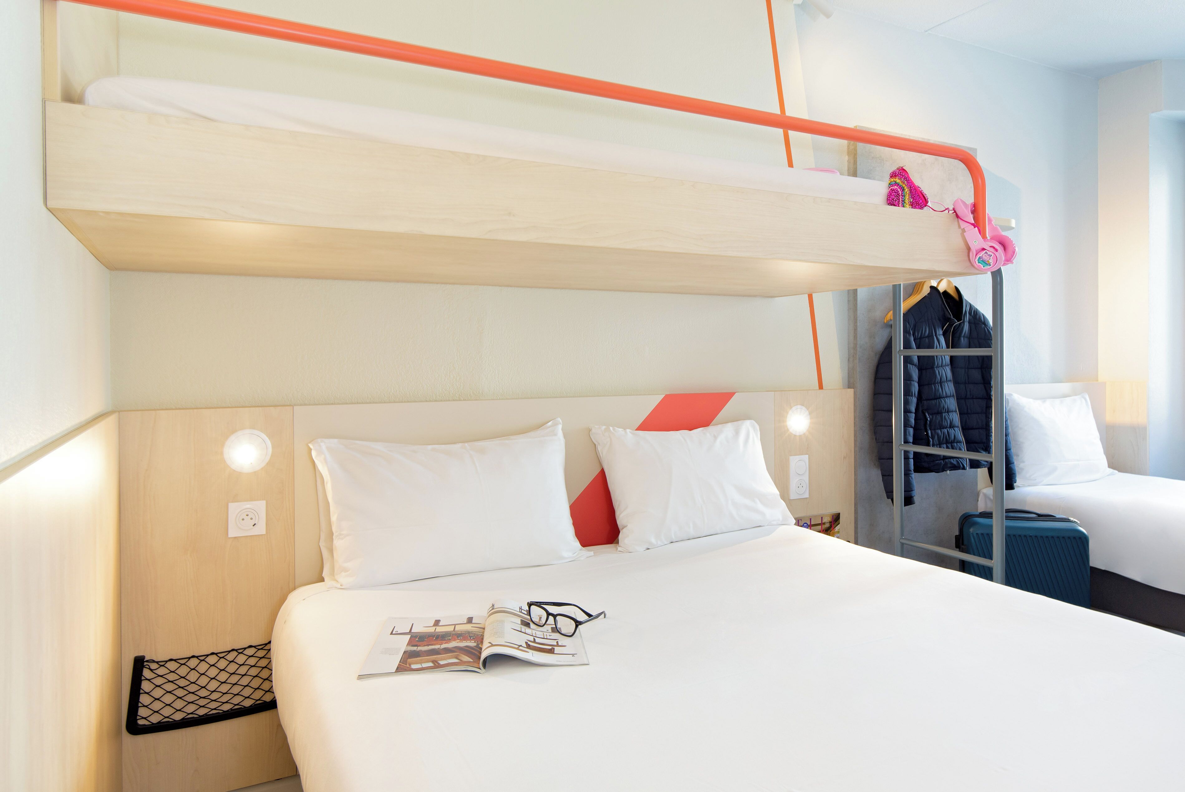 Ein Hotelzimmer mit Etagenbett, Schreibtisch, Stuhl, Koffer und Kleiderhaken.