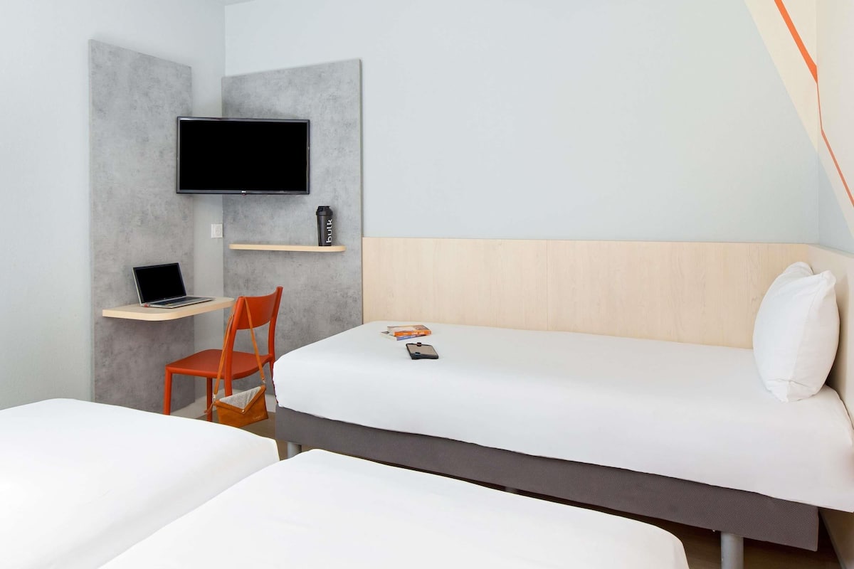 Een hotelkamer met een bed, een bureau met een laptop, een stoel, een aan de muur bevestigde televisie en een plank met een waterfles.