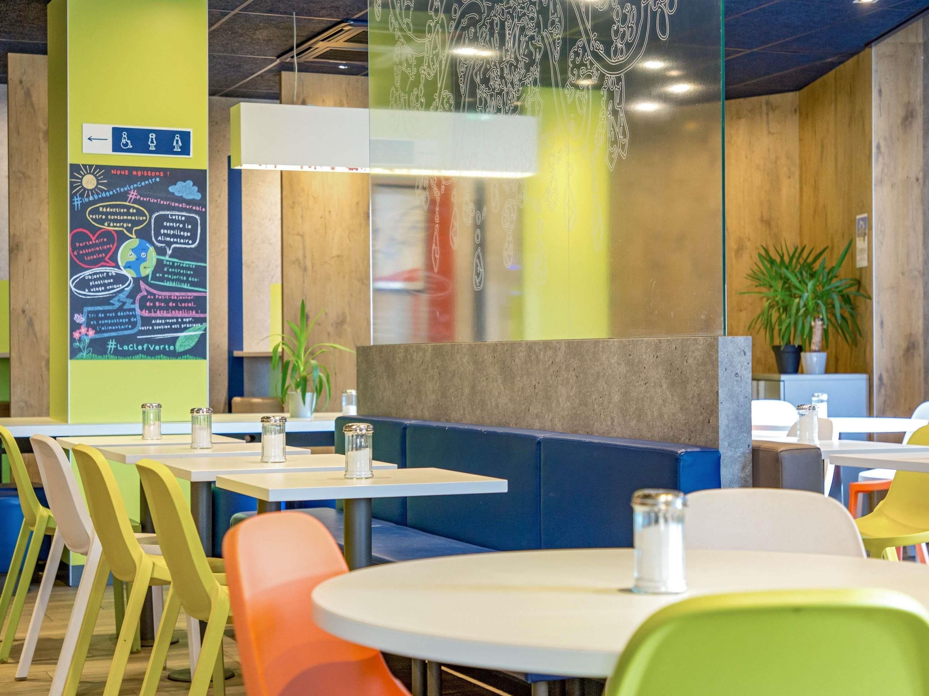 A modern restaurant with colorful chairs, tables, and a green wall with a poster.