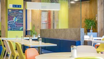 A modern restaurant with colorful chairs, tables, and a green wall with a poster.