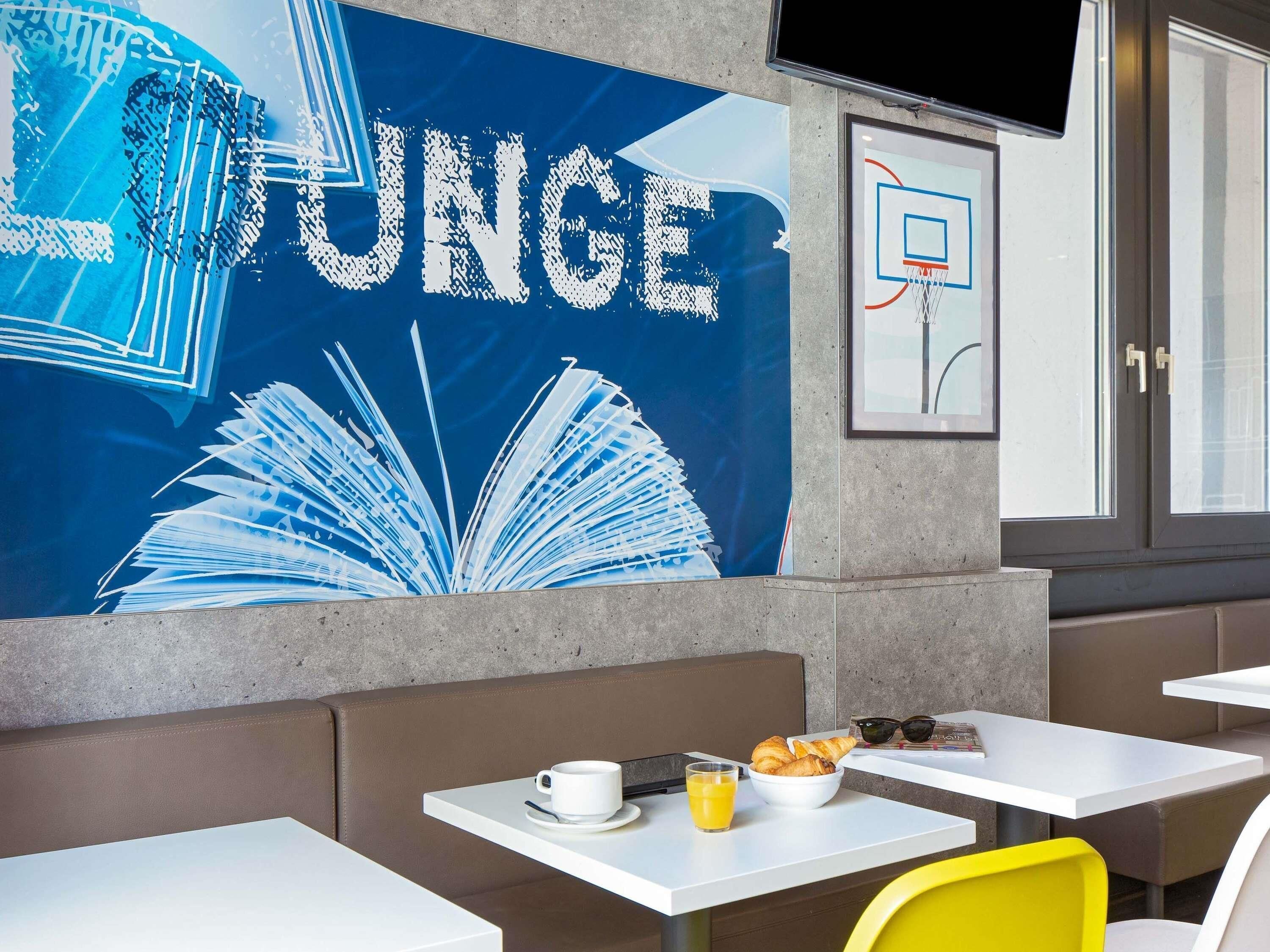A lounge area with a large wall mural, tables with breakfast items, and a framed basketball court diagram.