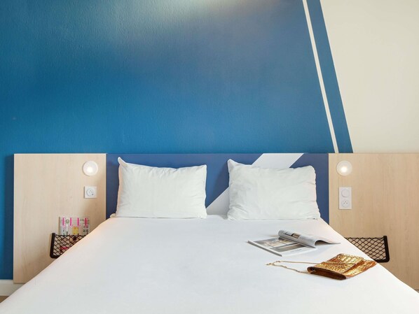 A hotel room with a bed, two white pillows, a magazine, a gold chain, and a black mesh bag.