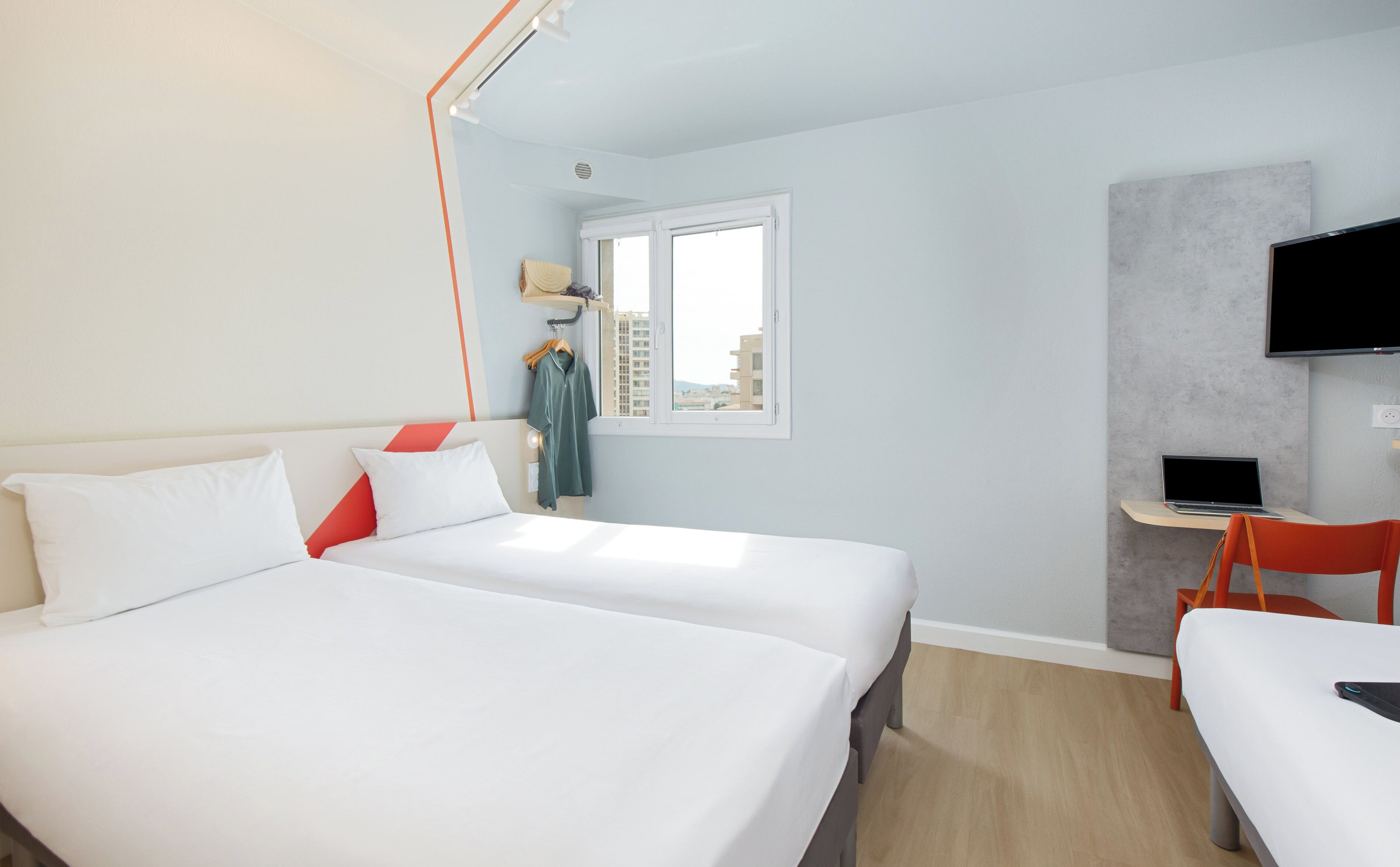 Ett hotellrum med två sängar, ett skrivbord med en bärbar dator, en tv och ett fönster med utsikt över staden.