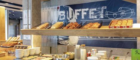 Een buffet met diverse etenswaren, zoals brood, gebak en ontbijtgranen.