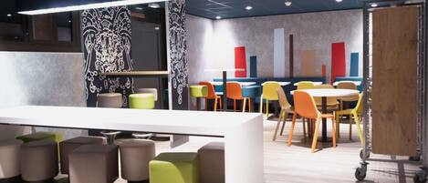 A modern restaurant with a long counter, colorful chairs, and a patterned wall.