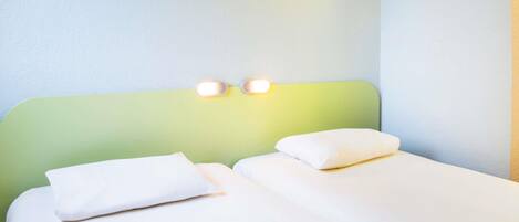 A hotel room with two single beds, a green headboard, and two wall-mounted lights.